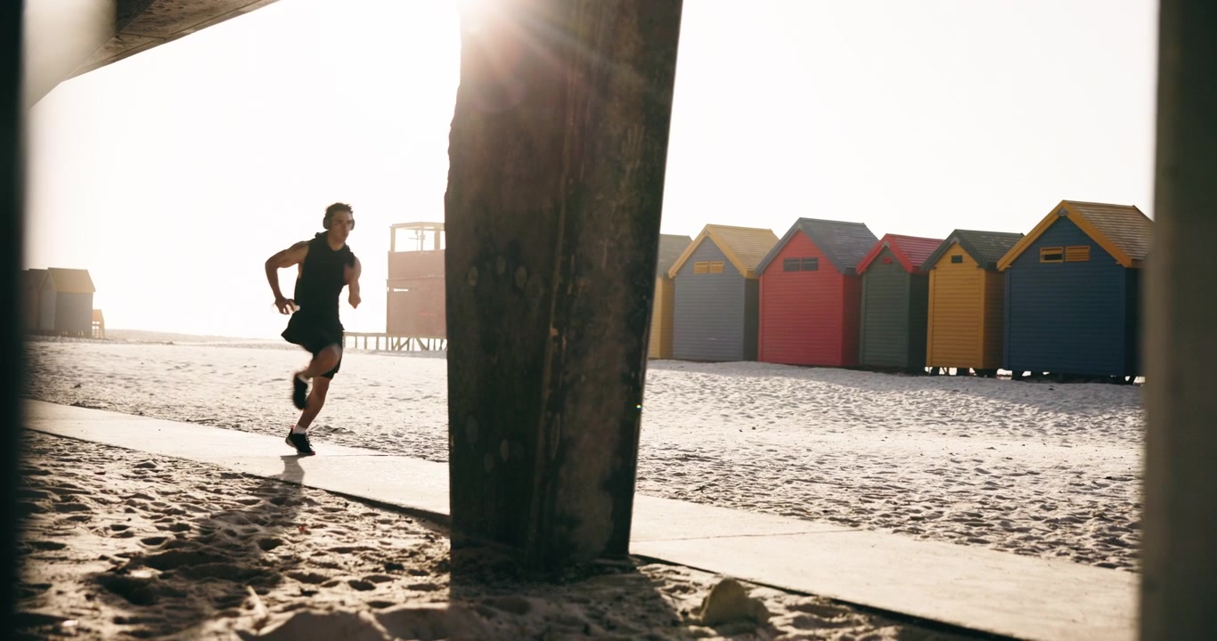 Giovane uomo che fa jogging davanti a variopinte cabine da spiaggia all'alba