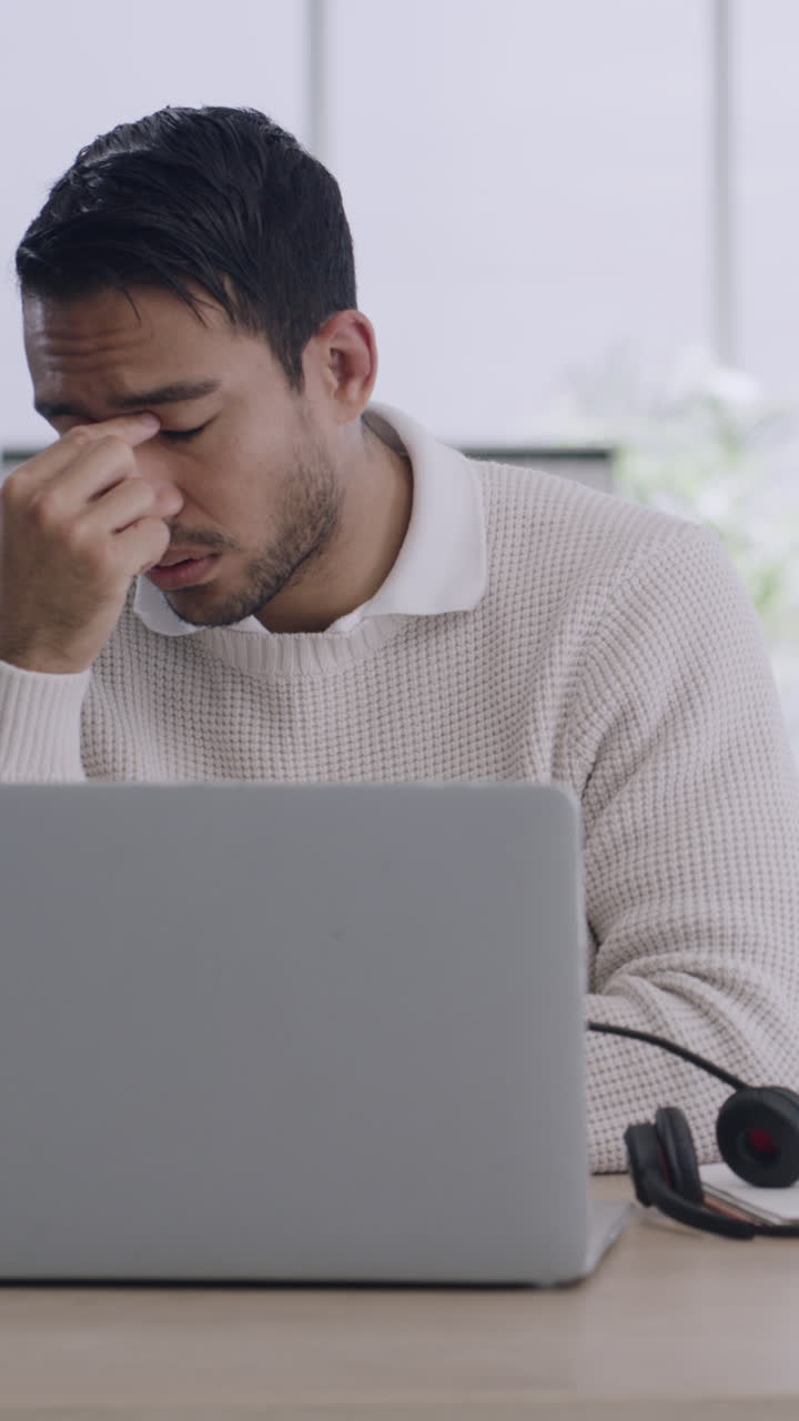 Stressed Man Removing Headset and Rubbing Temples While Working on Laptop