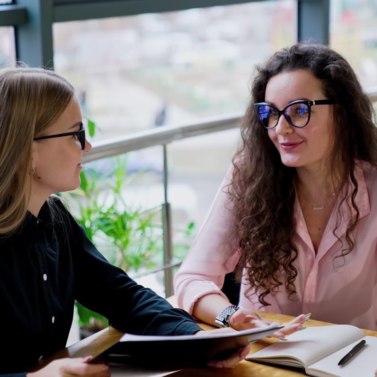 Women in office talking over business issues. Happy smiling ladies sit at the table with laptop and documentation