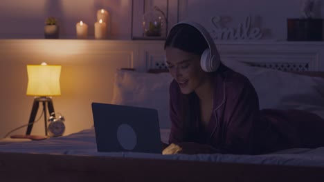 woman relaxing in bed with laptop and headphones