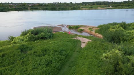 a girl walking towards the river shore, aerial pull back