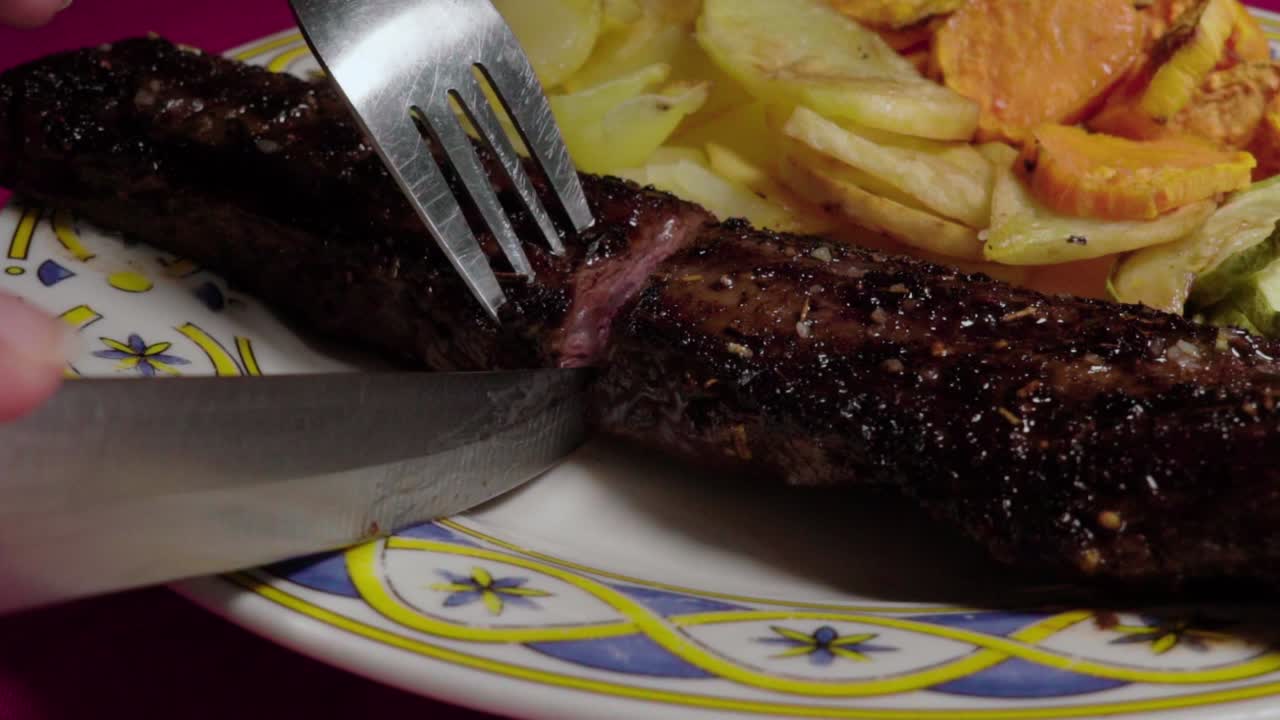 Primo piano: Tagliare una bistecca di manzo marinata e mostrarne l'interno con coltello e forchetta.