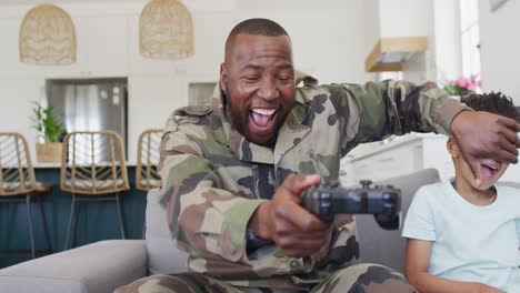 happy african american father and his son sitting on sofa and playing video games