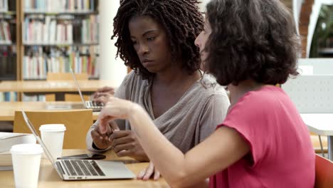 mujeres enfocadas usando laptop en la biblioteca