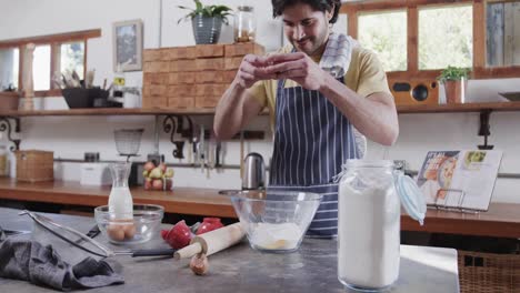 hombre caucásico feliz preparando masa de pan usando una tableta en la cocina, en cámara lenta