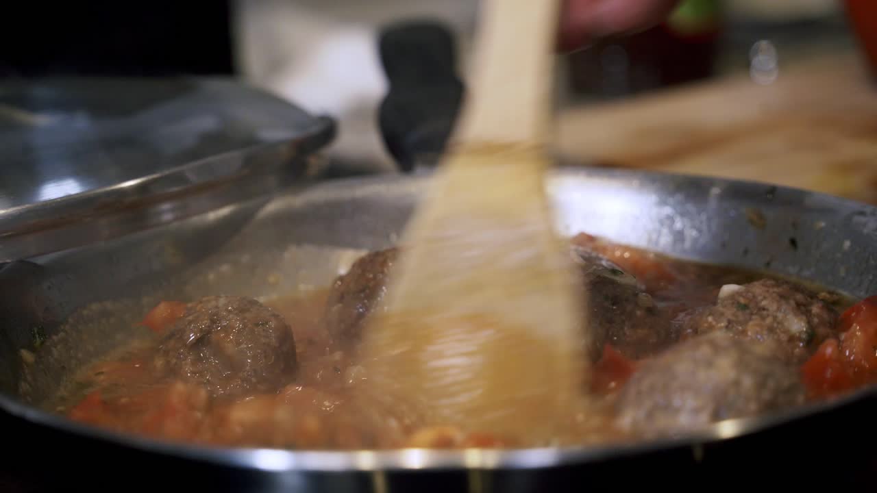 panning down on hand of person coking meatballs in pan Preparing ingredients to make vegan beyond meatballs with spaghetti and meat sauce