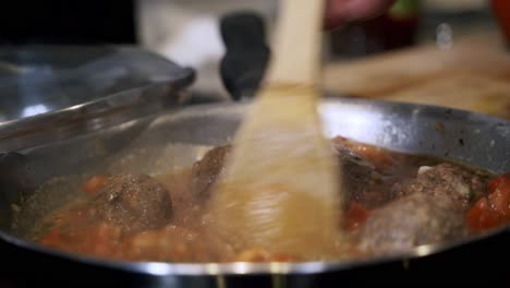 panning down on hand of person coking meatballs in pan preparing ingredients to make vegan beyond meatballs with spaghetti and meat sauce