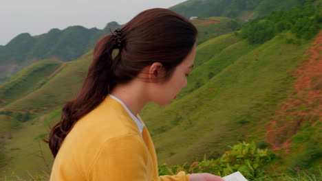 slow camera orbit around a woman reading on a hillside with her hair blowing in the wind