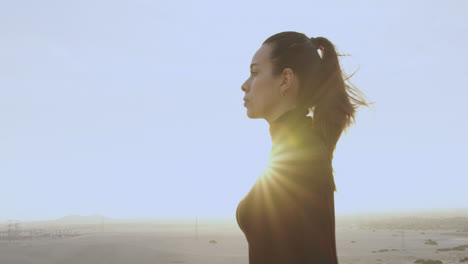 hermosa mujer de perfil vestida de negro y con el pelo atado mira hacia adelante en medio del desierto al atardecer contra el sol