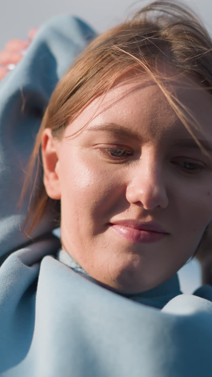 atleta en suéter azul participando en ejercicio de fitness, estirando los brazos por encima de la cabeza con una cálida sonrisa, la luz del sol destaca su cara bajo un cielo azul claro