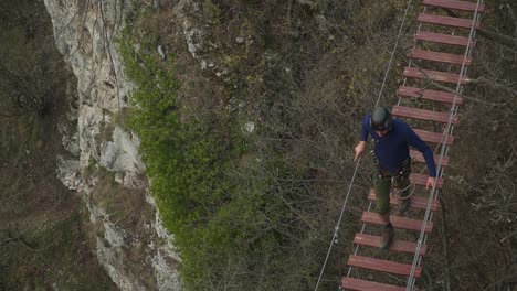 A tourist experiencing a walk on the wooden hanging bridge in Via ferrata, located in the Alps - tilt down