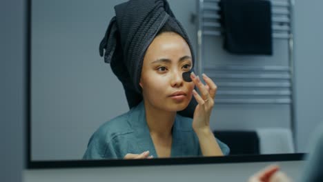 woman applying charcoal eye patches