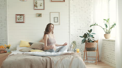 mulher grávida saudável a praticar ioga na cama, grávida a meditar dentro de casa.