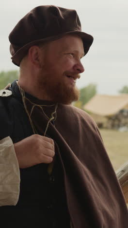 bearded village squire laughs and chats holding bottle of magic potion in bosom. positive medieval man rests on sunny day closeup on blurred background