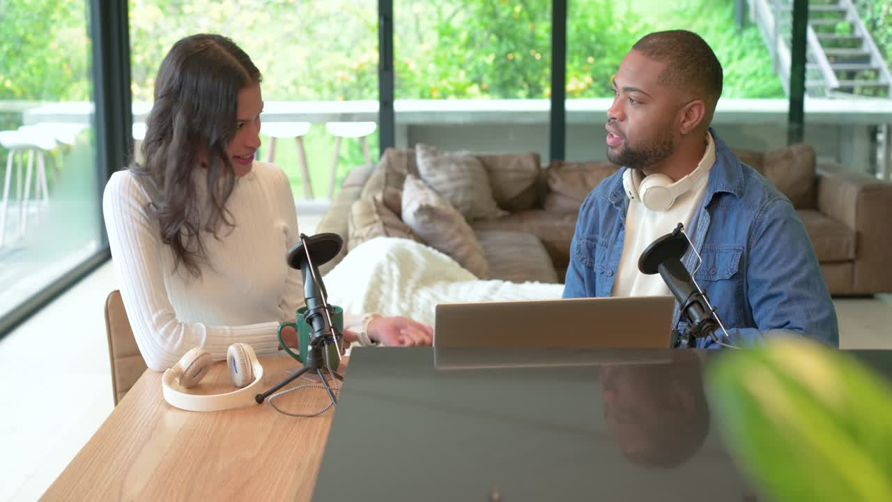 African American man adjusting mic at home, Asian woman entering with green mug to talk
