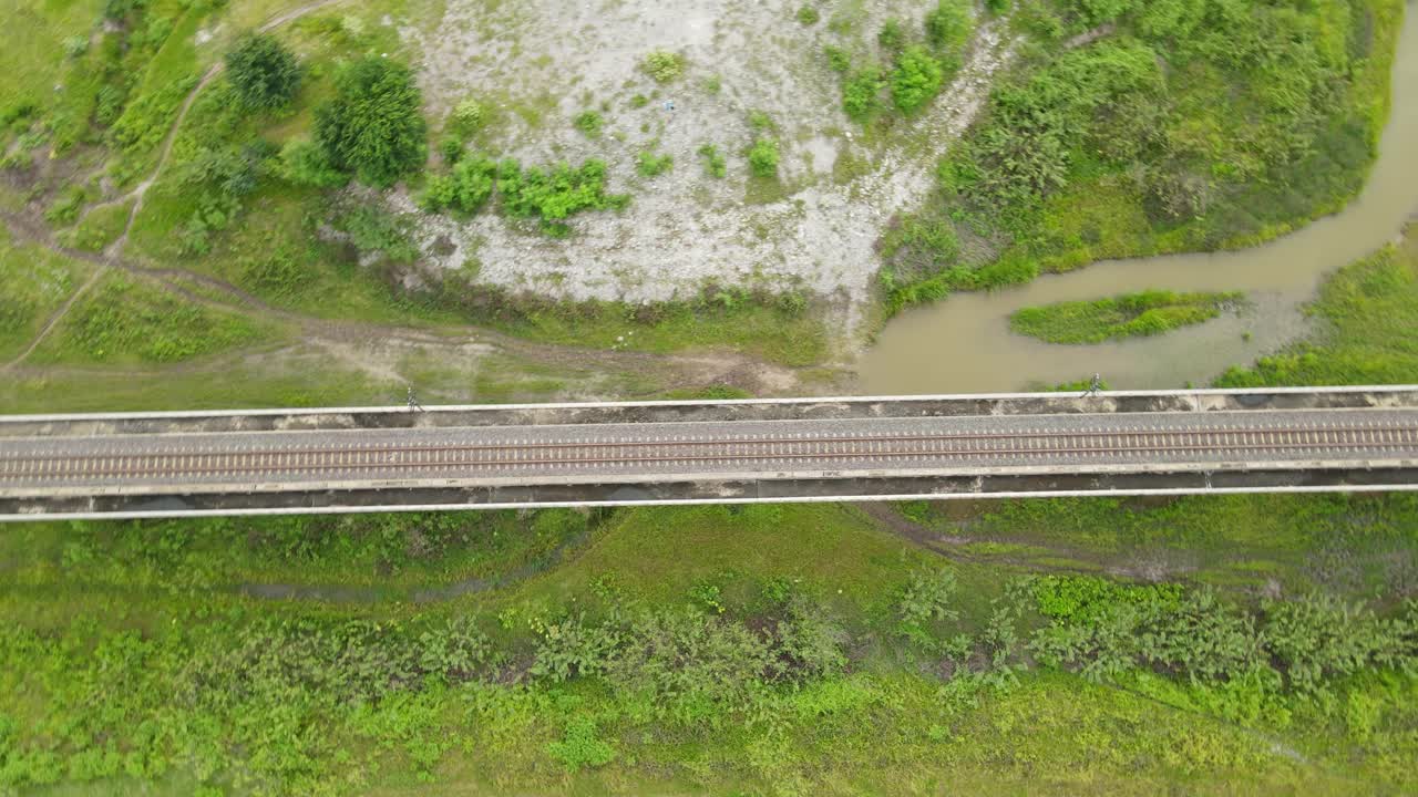 A spinning aerial footage revealing the elevated railroad, grass land with water and dirt roads; Muak Klek, Saraburi, Thailand
