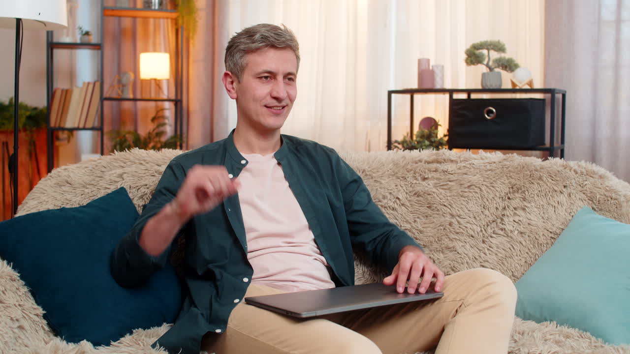Young man closes laptop with smile and shows victory gesture after finishing productive online work