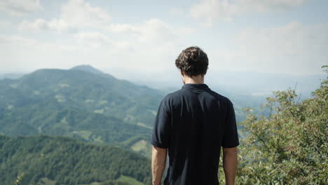 man, wearing dark shirt, looking ito the valley from peak of the mountain