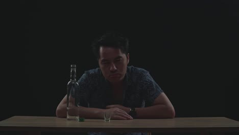 drunk asian man with vodka looking at camera in black background