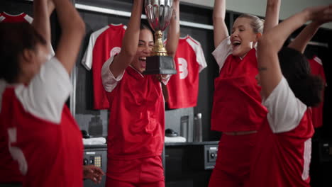 women's team celebrating victory in locker room with trophy