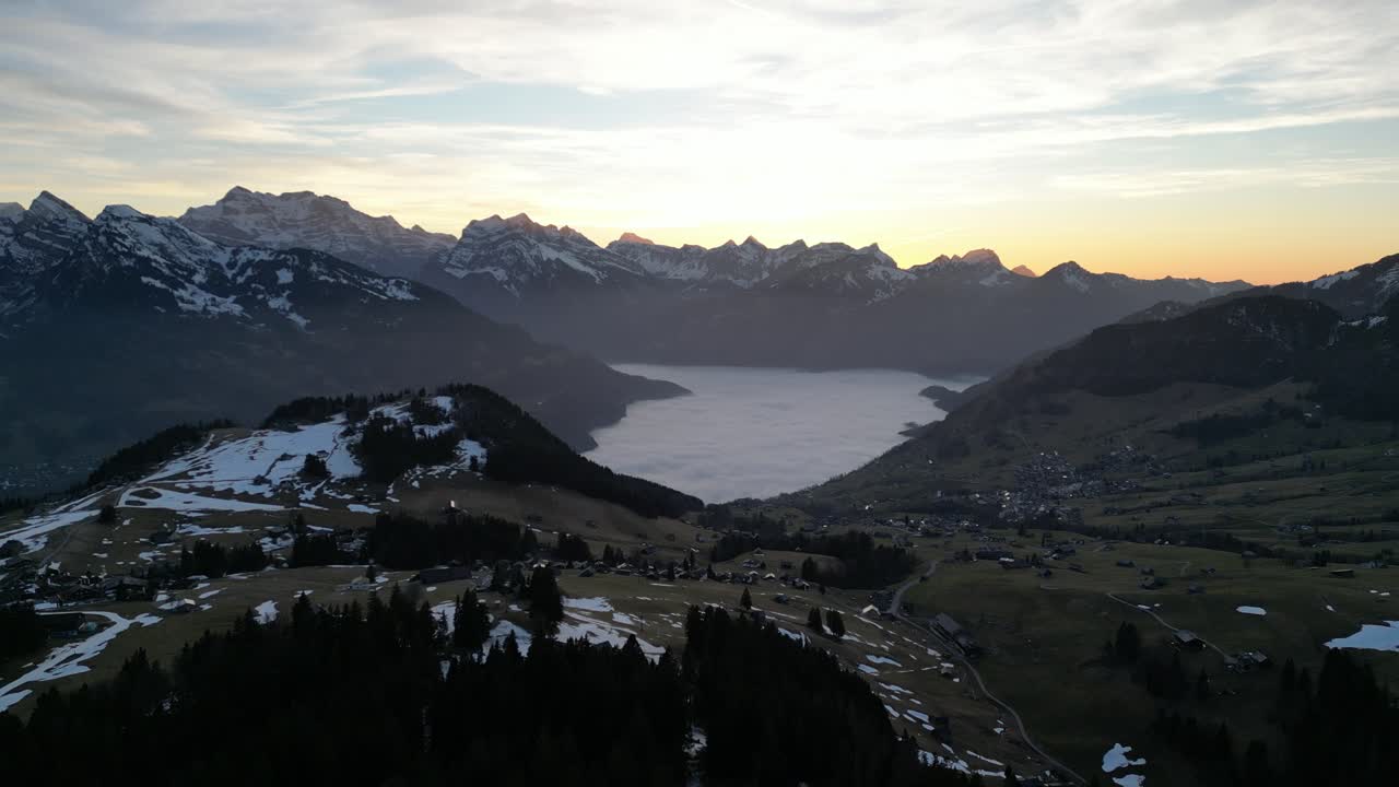 dolly aéreo por encima de la cresta con neblina amarilla naranja y nubes finas en el horizonte, lago walen walensee suiza