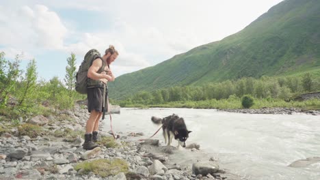 Männlicher-Rucksacktourist-Mit-Einem-Hund-Hält-Vom-Gehen-Ab-Kühlt-Seinen-Körper-Mit-Wasser-Aus-Einem-Felsigen-Fluss-Im-Lyngsdalen-tal,-Norwegen