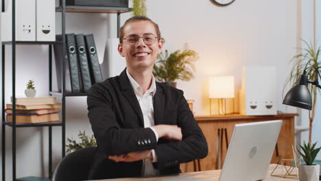 smiling young caucasian businessman freelancer showing double thumbs up sitting at home office desk