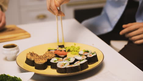 close view of a plate of sushi and hands holding japanese chopsticks