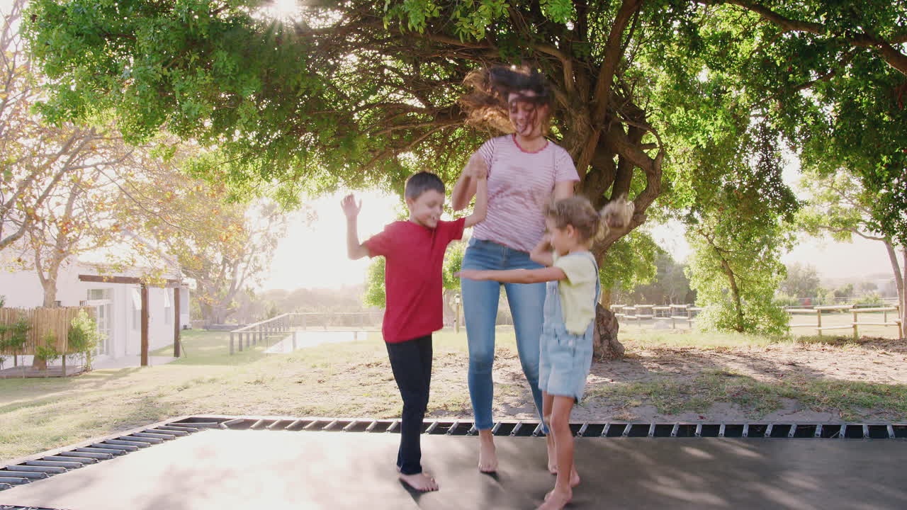 hermanos con hermana adolescente jugando en el trampolín al aire libre en el jardín