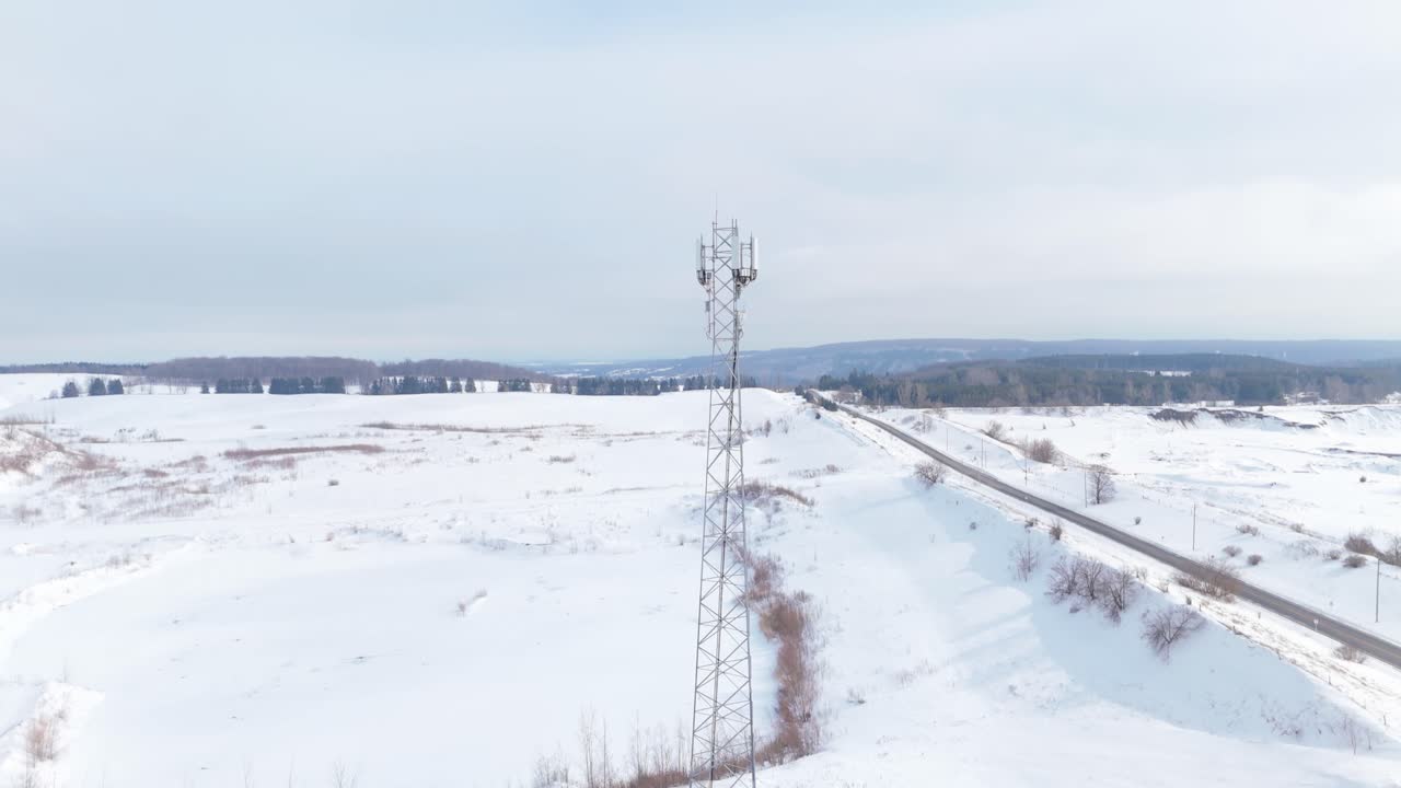 Torre di telecomunicazioni accanto a una strada in un paesaggio invernale ghiacciato, ripresa aerea in tilt.