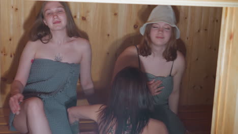 three women tying towels carefully, sitting on wooden bench in sauna, looking around in peaceful, serene moment after bath or shower, enjoying relaxing wellness time in natural setting