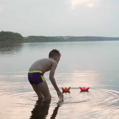 little boy launch paper ship on the water. beautiful summer sunset. paper boat. origami.