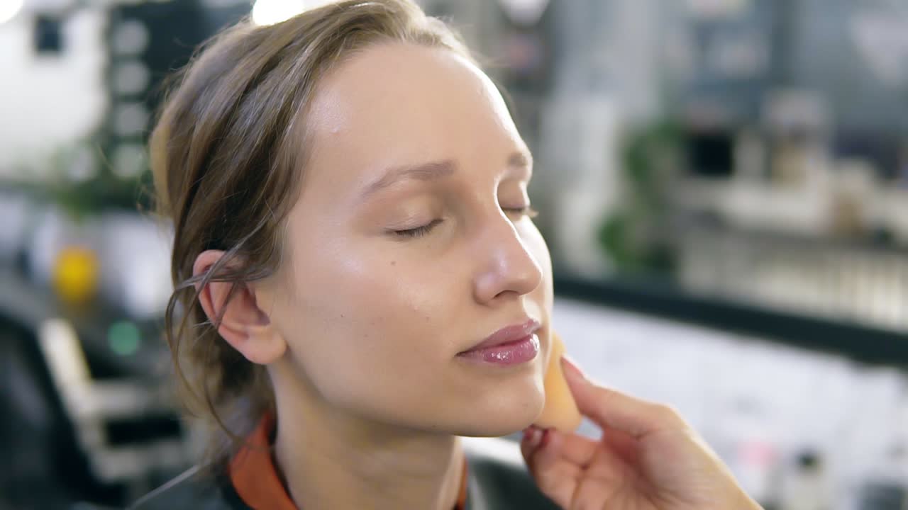 Close up of a young woman's face and artist hand putting on the tone with a sponge. Natural beauty. Studio