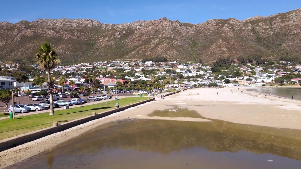 Spiaggia principale di Gordon's Bay con piscina di marea che riflette le montagne Hottentots Holland e le proprietà sul fianco della montagna. Ripresa aerea in elevazione.