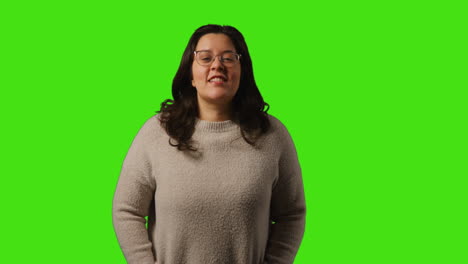 retrato de estudio de una mujer joven sonriente vestida casualmente con gafas de pie contra el fondo de la pantalla verde