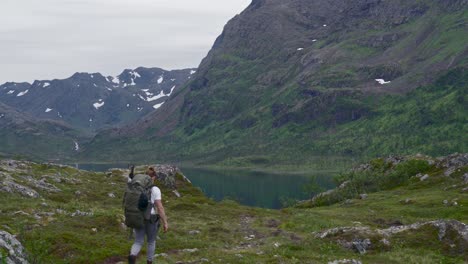 mochilero caminando hacia el lago junto a la montaña en noruega durante el invierno, tiro amplio, estático