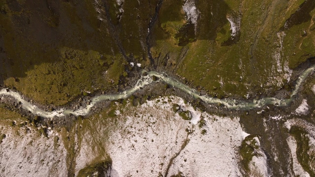 Aerial birds eye shot of a glacier river in a snowy valley coming from Sólheimajökul in Iceland.