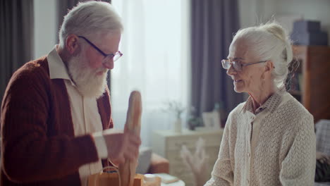 senior man unpacking groceries at home with help from wife
