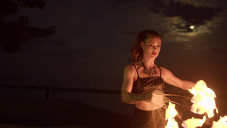 Woman-Twirling-And-Waving-Fire-Fans-Against-Cloudy-Moon-Lit-Sky,-Medium-Shot-Slowmo