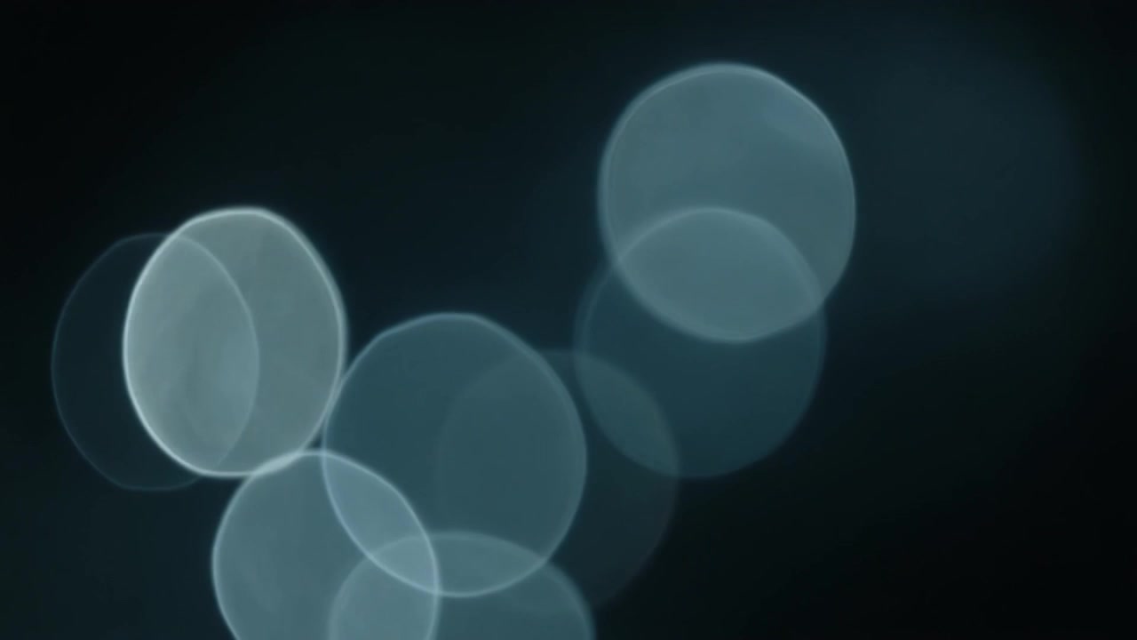 Abstrakte blå bokeh-lyskuler som beveger seg på mørk bakgrunn
