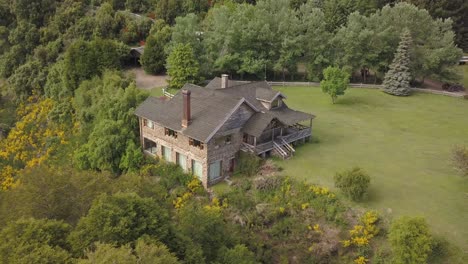 Aerial-orbiting-shot-of-old-stony-house-standing-on-hill-surrounded-by-trees-in-Patagonia,-Argentina