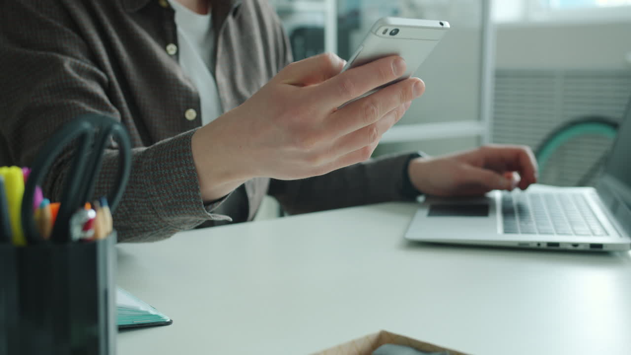 Person using smartphone and laptop at their desk