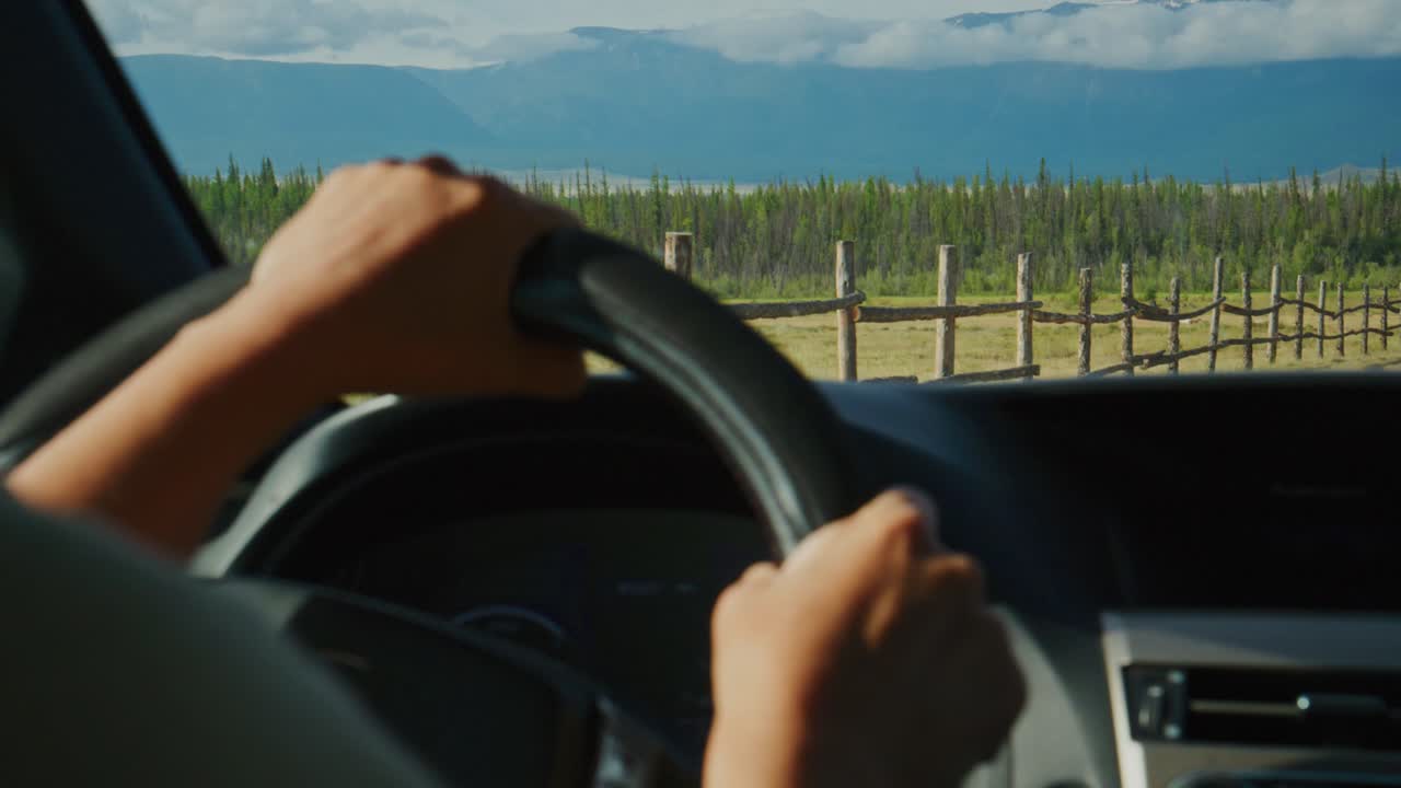 L'autista stringe il volante, occhi fissi in avanti. Il paesaggio montuoso si estende davanti. La strada si snoda oltre una recinzione di legno, filari di vigneti. Cielo azzurro limpido, guida tranquilla. Perfetto per viaggi, avventura, road trip.