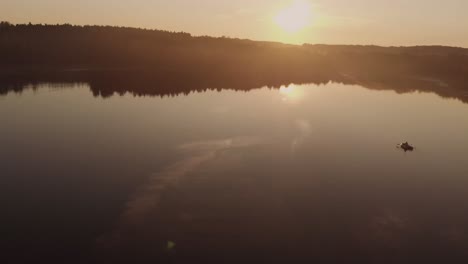 Persona-Remando-En-Un-Bote-Inflable-En-Aguas-Tranquilas-Y-Tranquilas-Del-Lago-En-Una-Puesta-De-Sol-Dorada-Cerca-Del-Pueblo-De-Rogowko,-Polonia