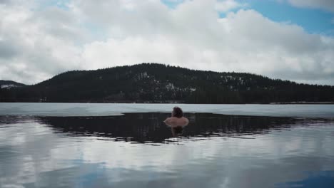 back view of a man swimming in freezing cold lake in winter