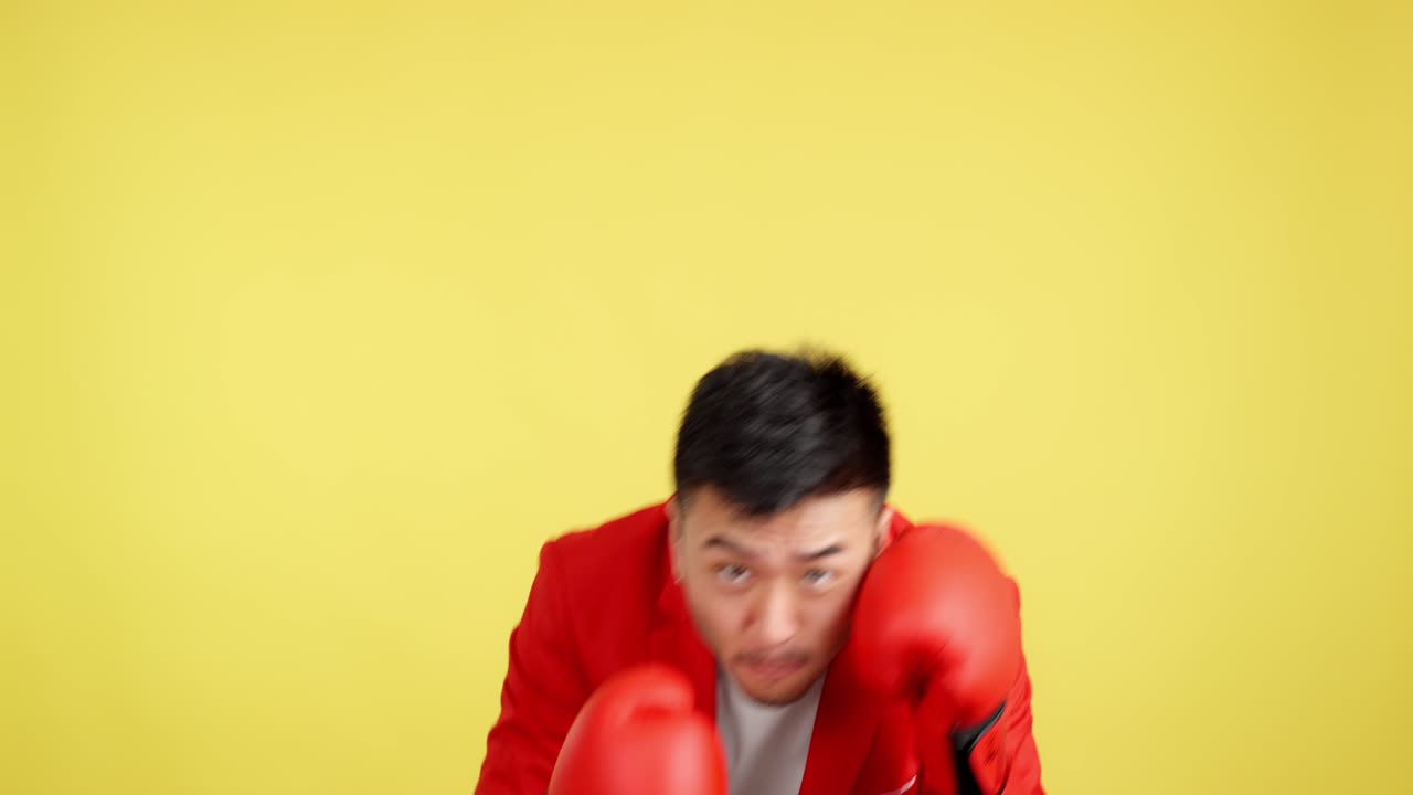 Man in red blazer and boxing gloves training against a yellow background