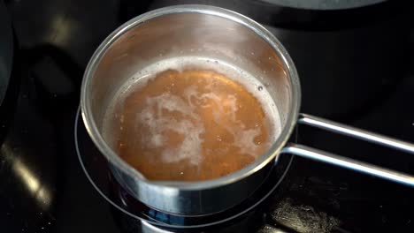 delicious golden bone broth simmering in small stainless steel pan, slow motion