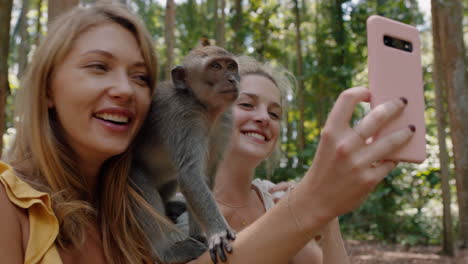 mejores amigas usando teléfonos inteligentes tomando fotos con un mono sentado en el hombro dos mujeres divirtiéndose posando con monos en el zoológico de vida silvestre turistas viajan a bali