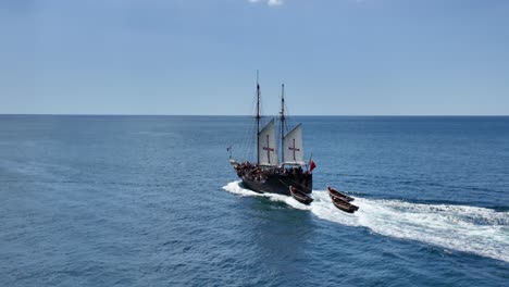 replica of a portuguese caravel sailing the ocean followed by three rowing boats in portugal