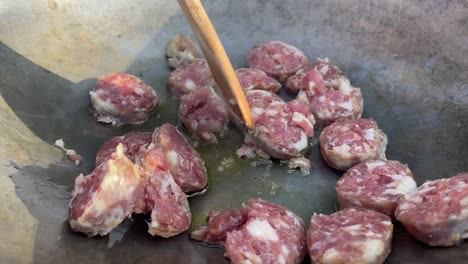 frying sausage in a wok over an open fire